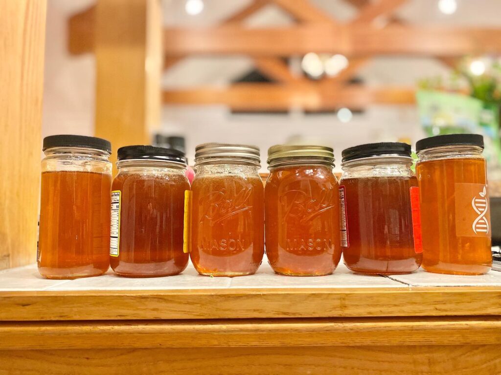 Six jars of honey on a wooden shelf